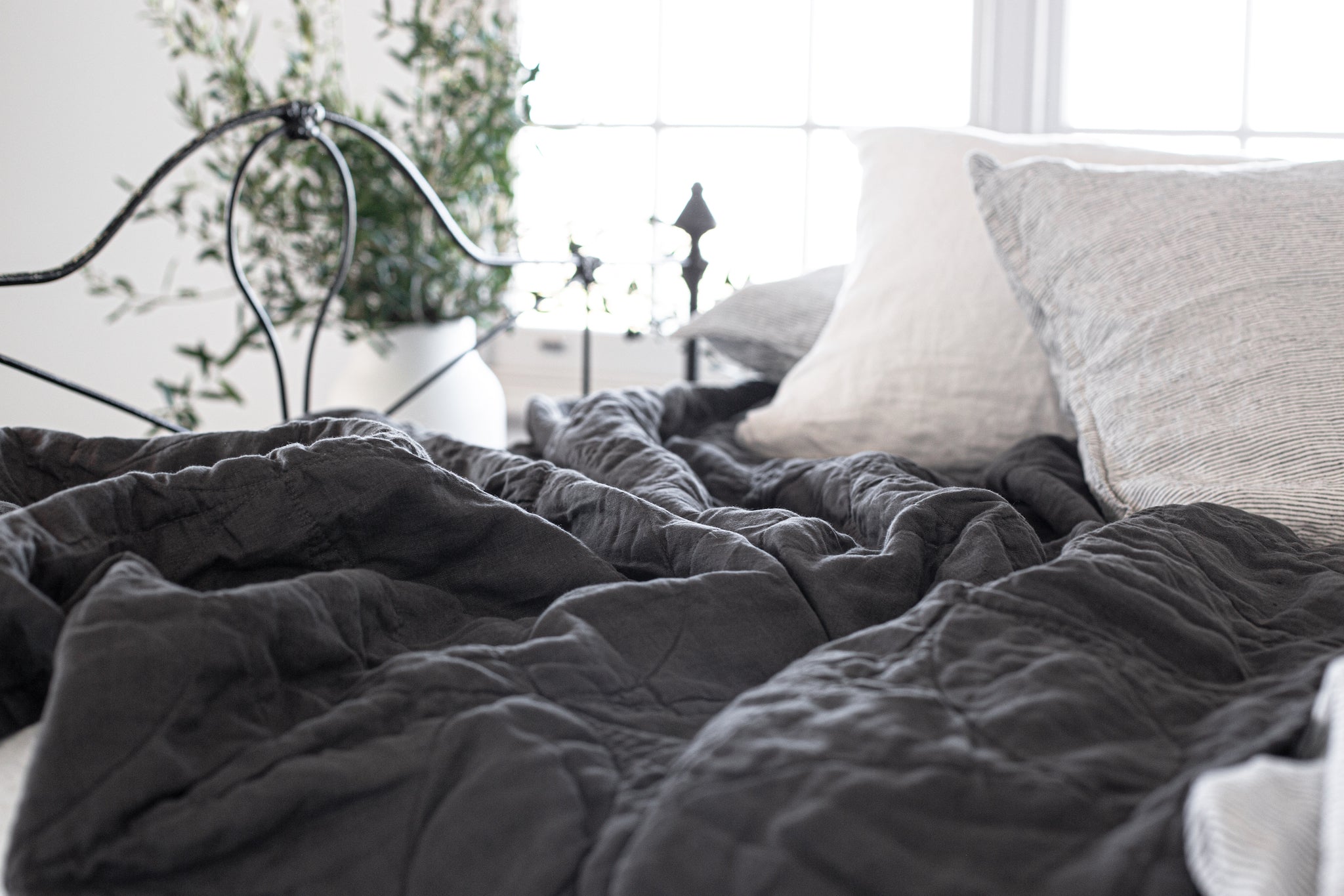 A dark charcoal linen blanket on a bed, with circle stitching visible and the blanket draped over the bed in a relaxed manner.