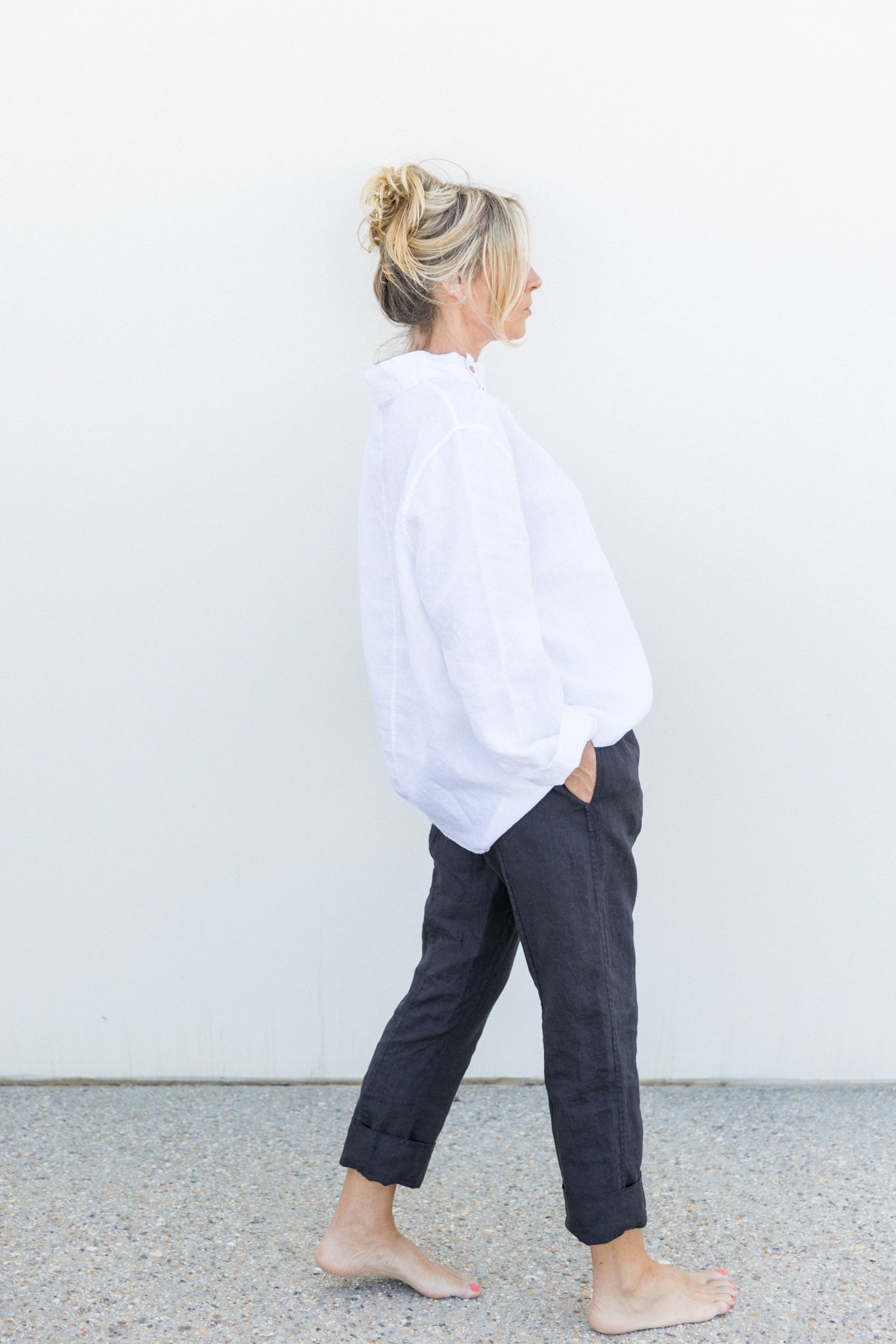 Woman in a white tunic top and dark blue trousers in front of a white wall