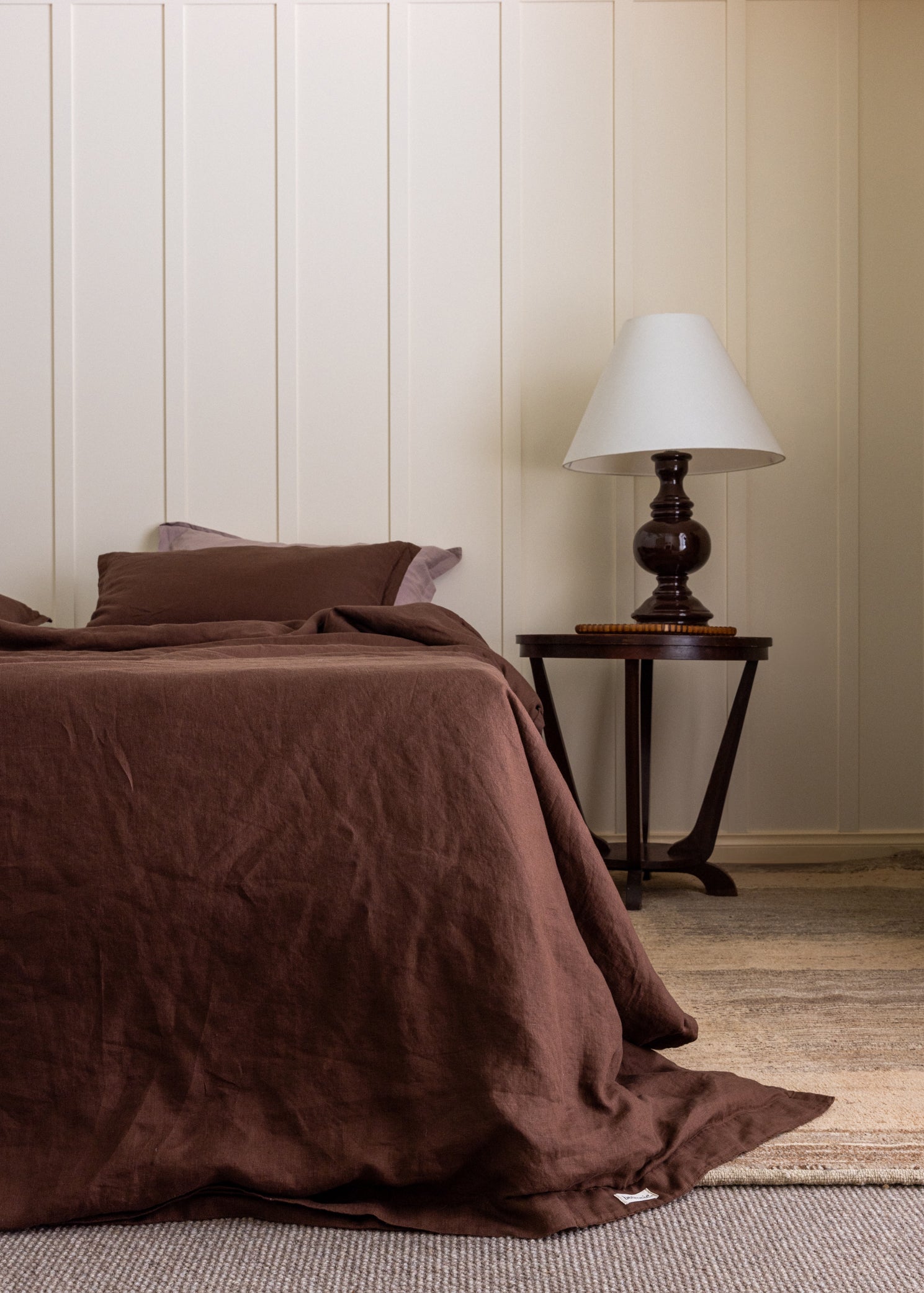 A brown duvet cover set on a bed, with a bedside table and lamp, in a room with light walls.
