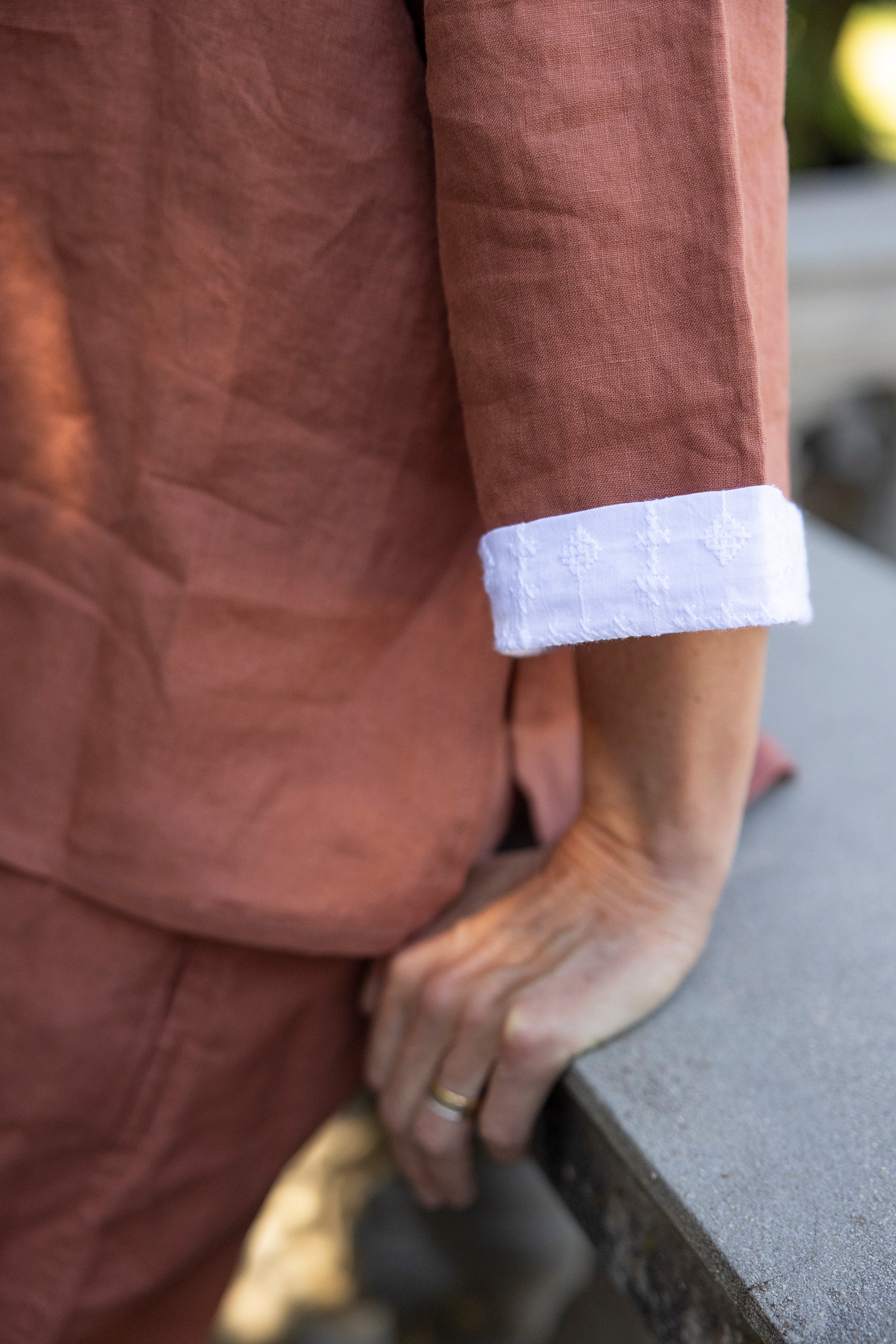 Person wearing a rust outfit with white cuffs, sitting on a concrete surface.