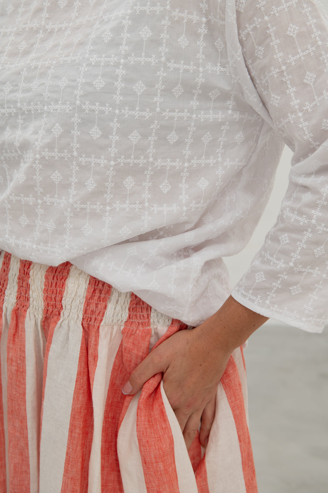 A person wearing an oversized white embroidered cotton top with a crew neckline and long sleeves, featuring a relaxed fit and drop shoulder silhouette.