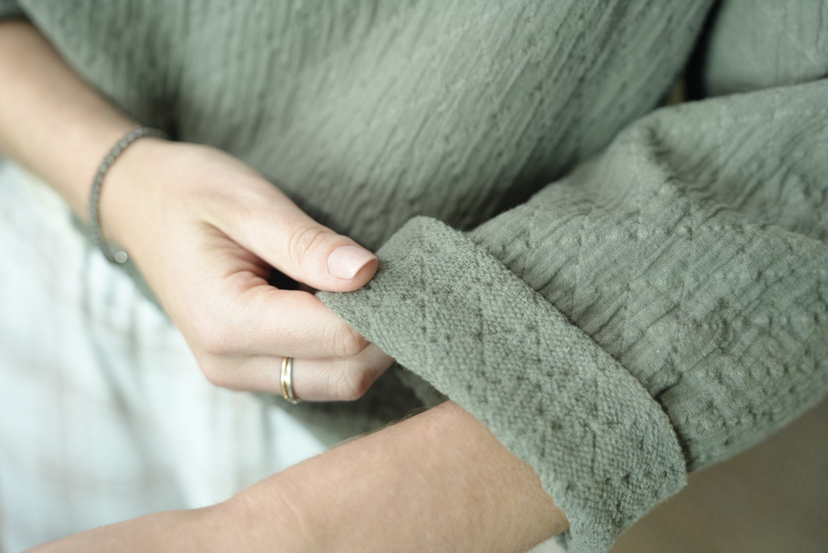 A close-up image of a person's hand rolling up a sleeve of a khaki-colored, textured cotton top.