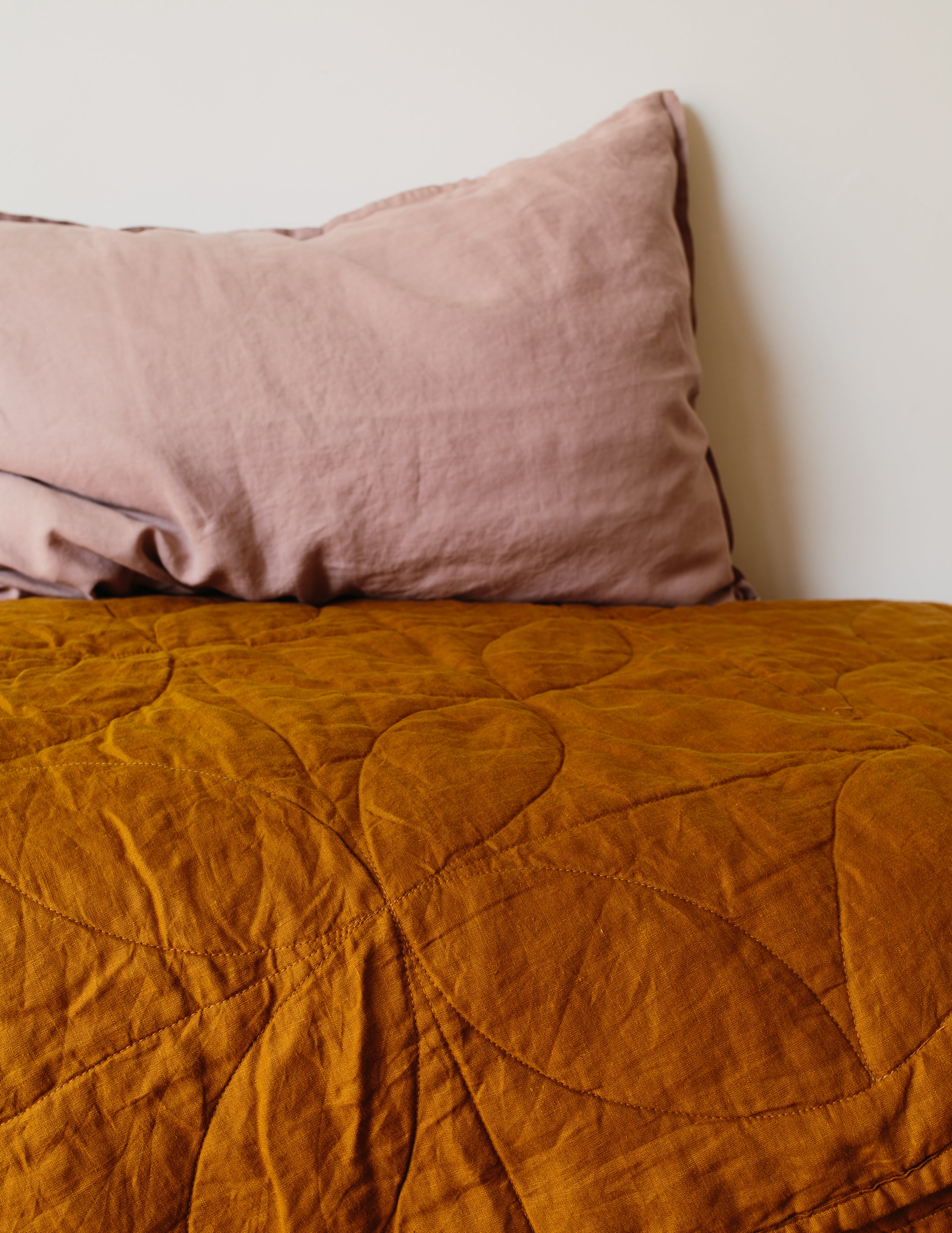 Pink pillow on a mustard yellow quilt against a white wall