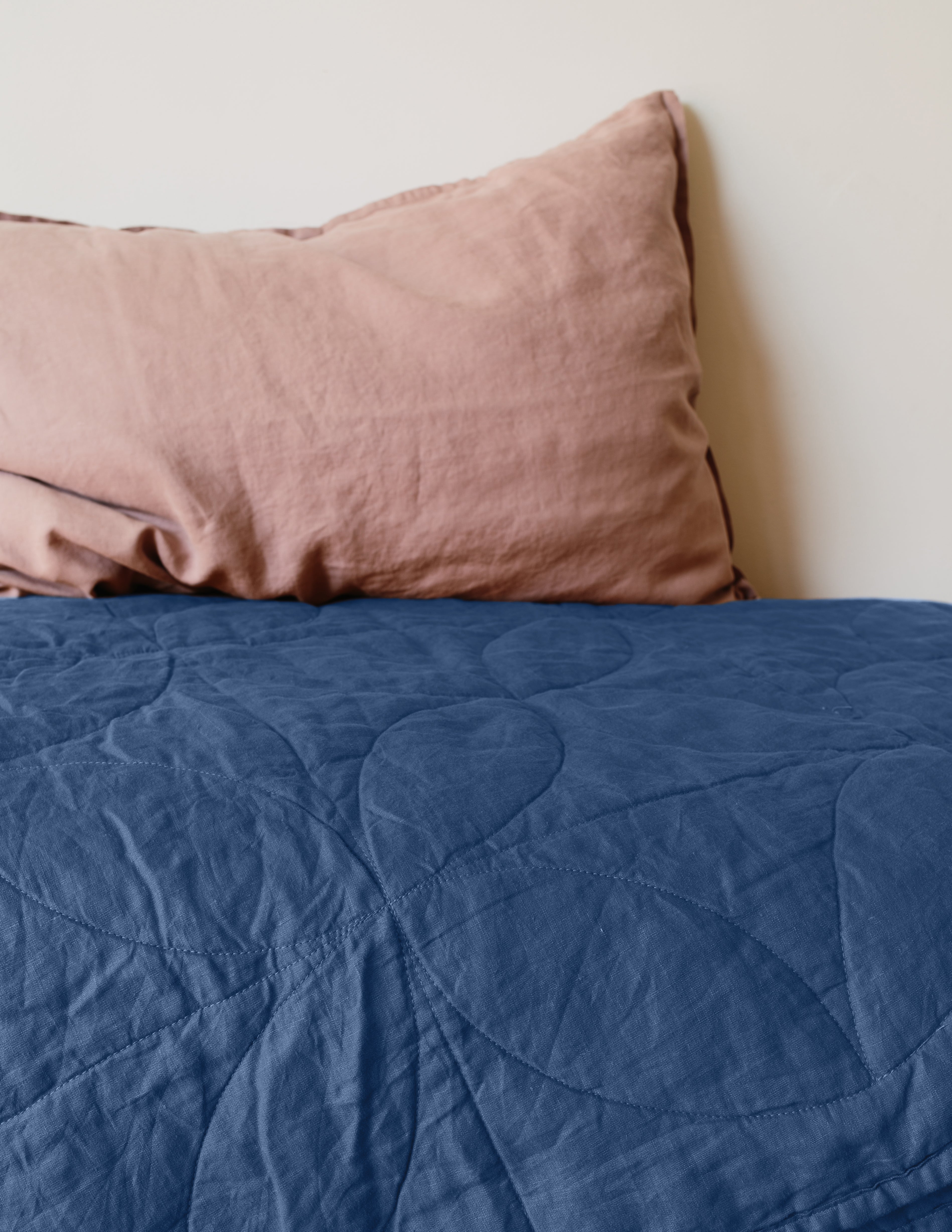 Blue quilted coverlet on a bed with a pink pillow against a white wall