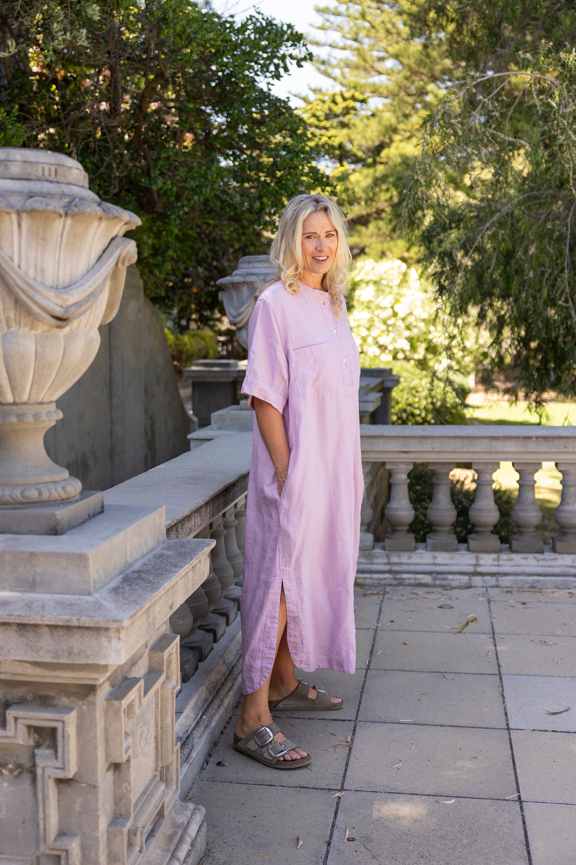 Woman in a light purple dress standing outdoors near classical architecture.