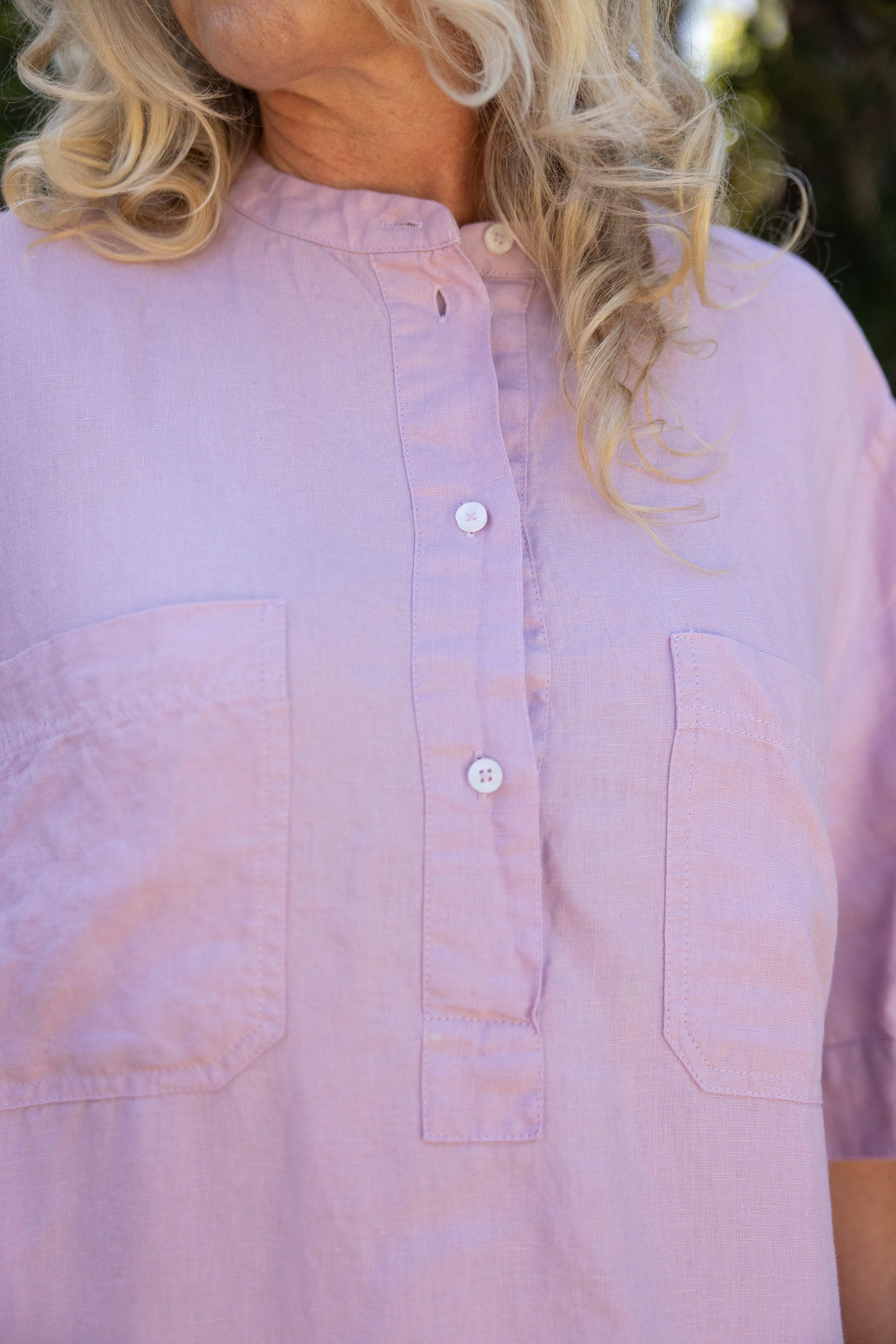 Close-up of a person wearing a light purple button-up shirt with a blurred background