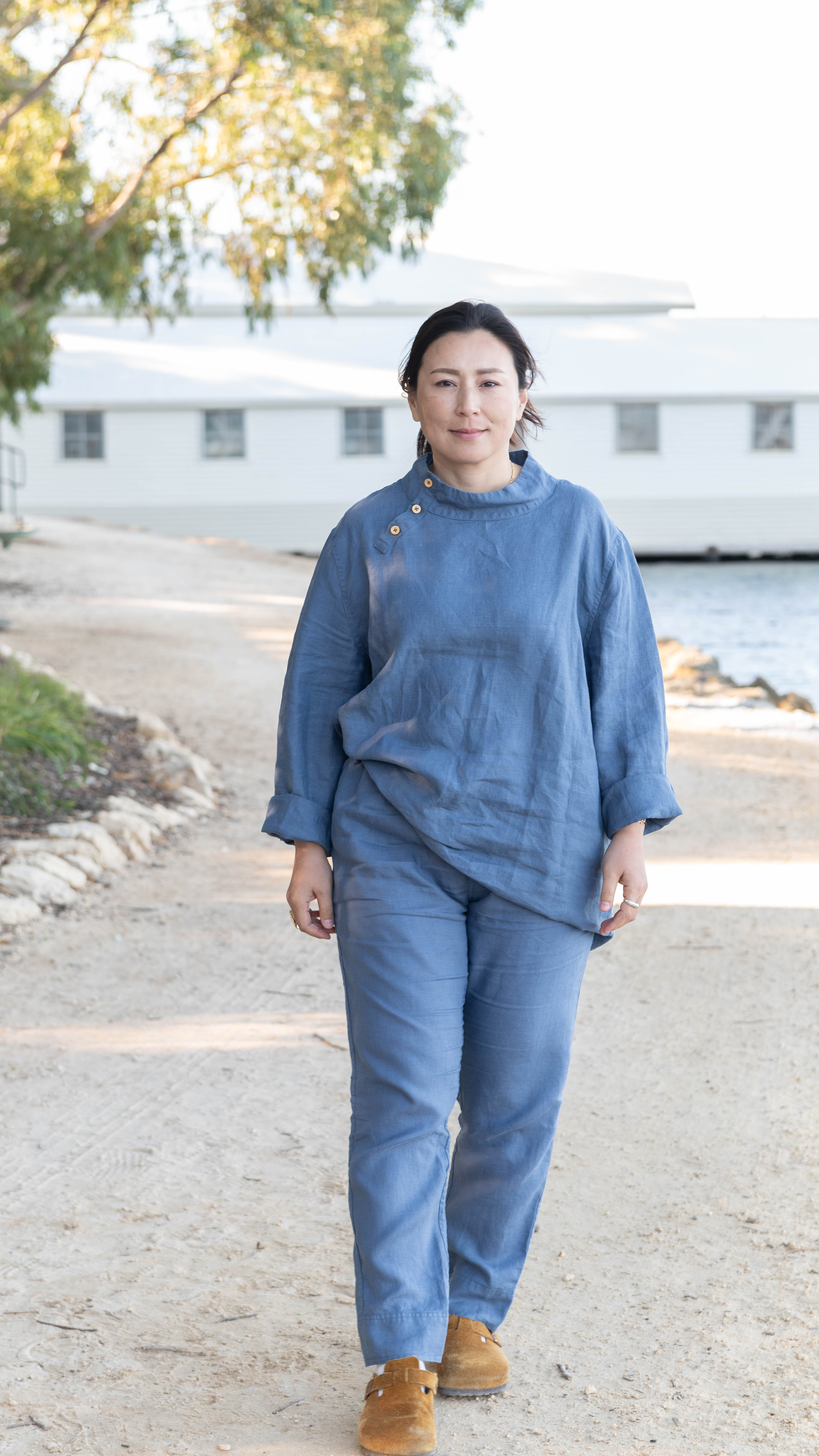 A person wearing a relaxed fit denim blue tunic with a stand-up turtleneck and long sleeves, paired with matching straight-leg trousers.