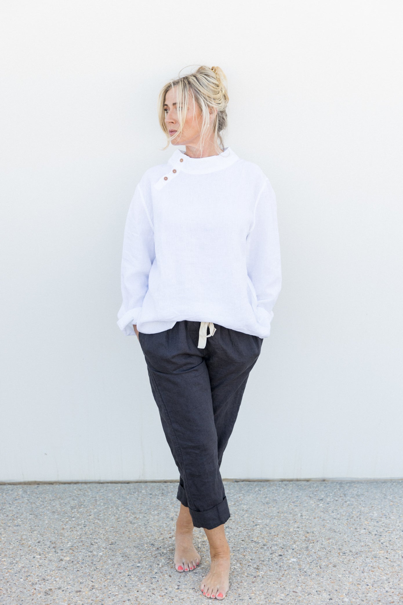 A person wearing a white tunic top and dark pants standing against a plain background.
