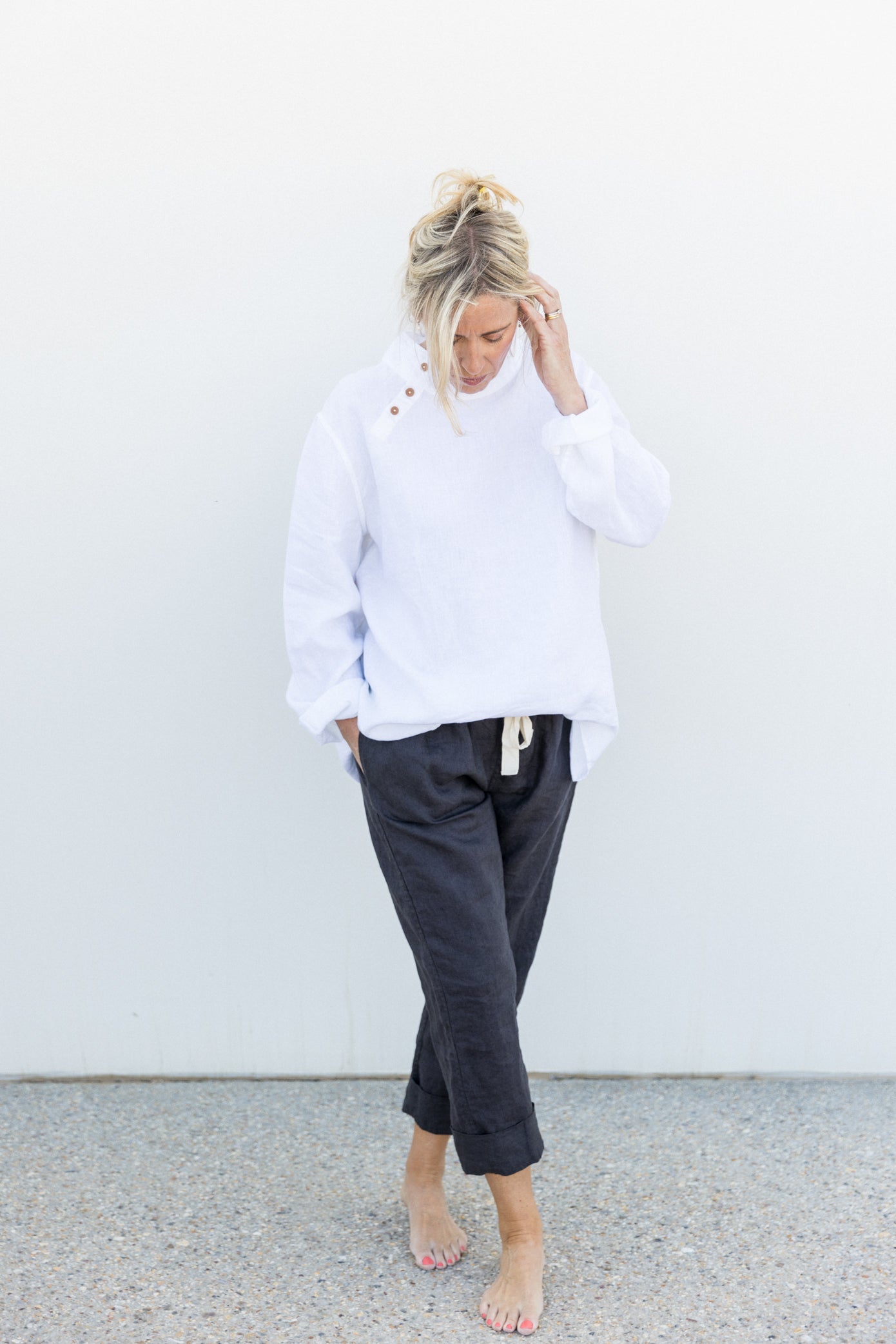 A person wearing a relaxed fit white tunic with a stand-up turtleneck and long sleeves, paired with dark blue straight-leg trousers.