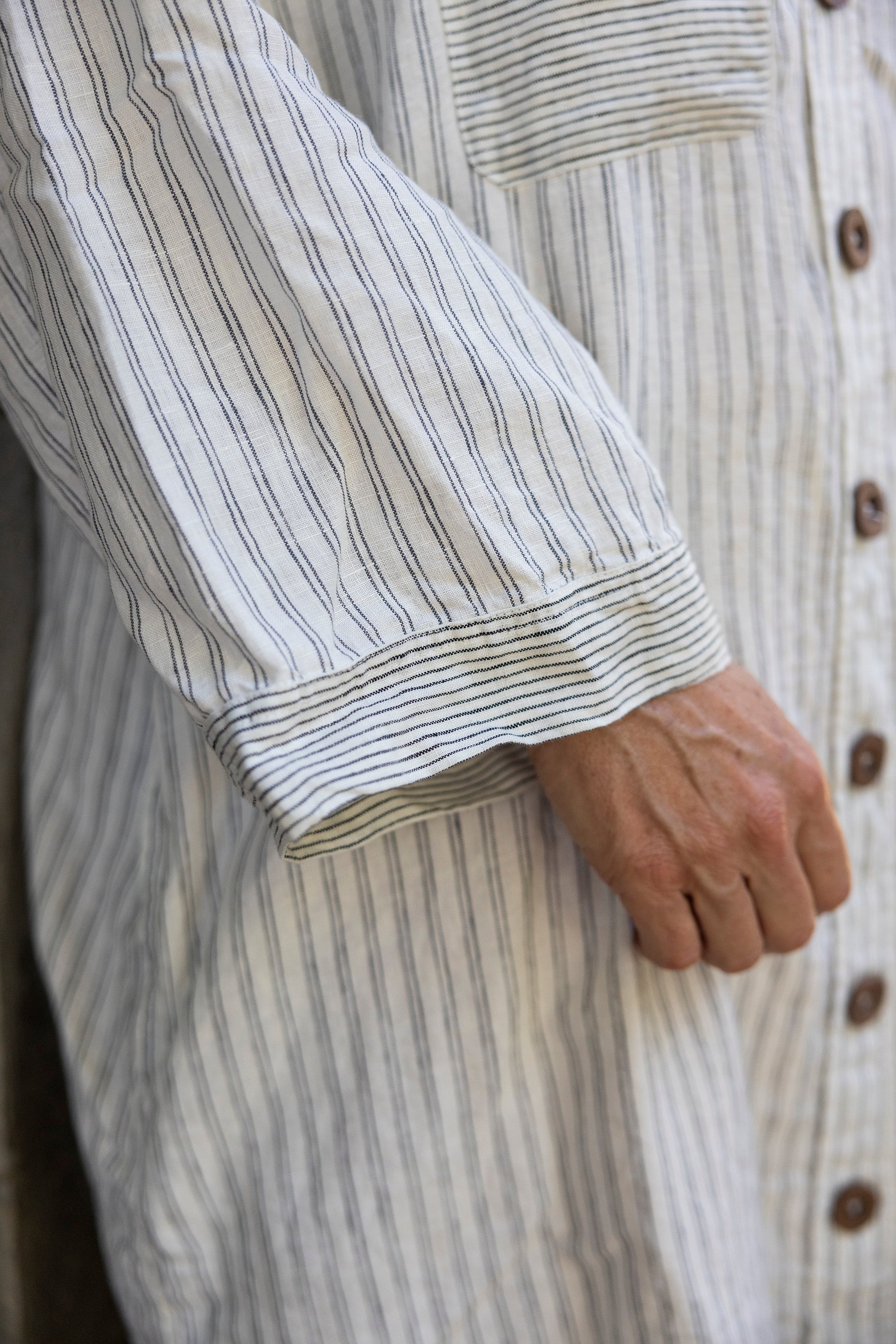 Close-up of a person wearing a long, striped shirt with a focus on the sleeve and hand.