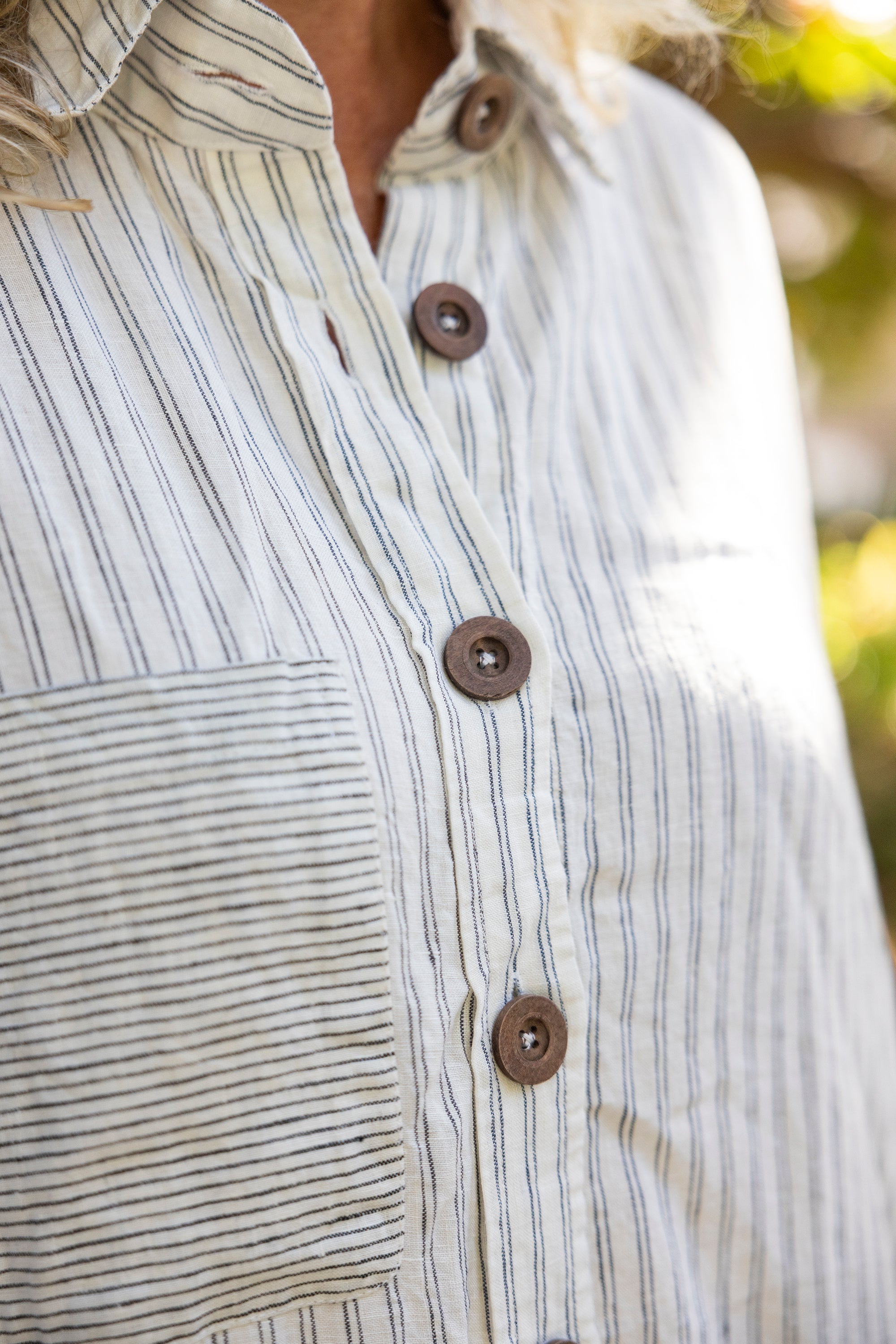 Close-up of a person wearing a striped shirt with brown buttons against a blurred natural background