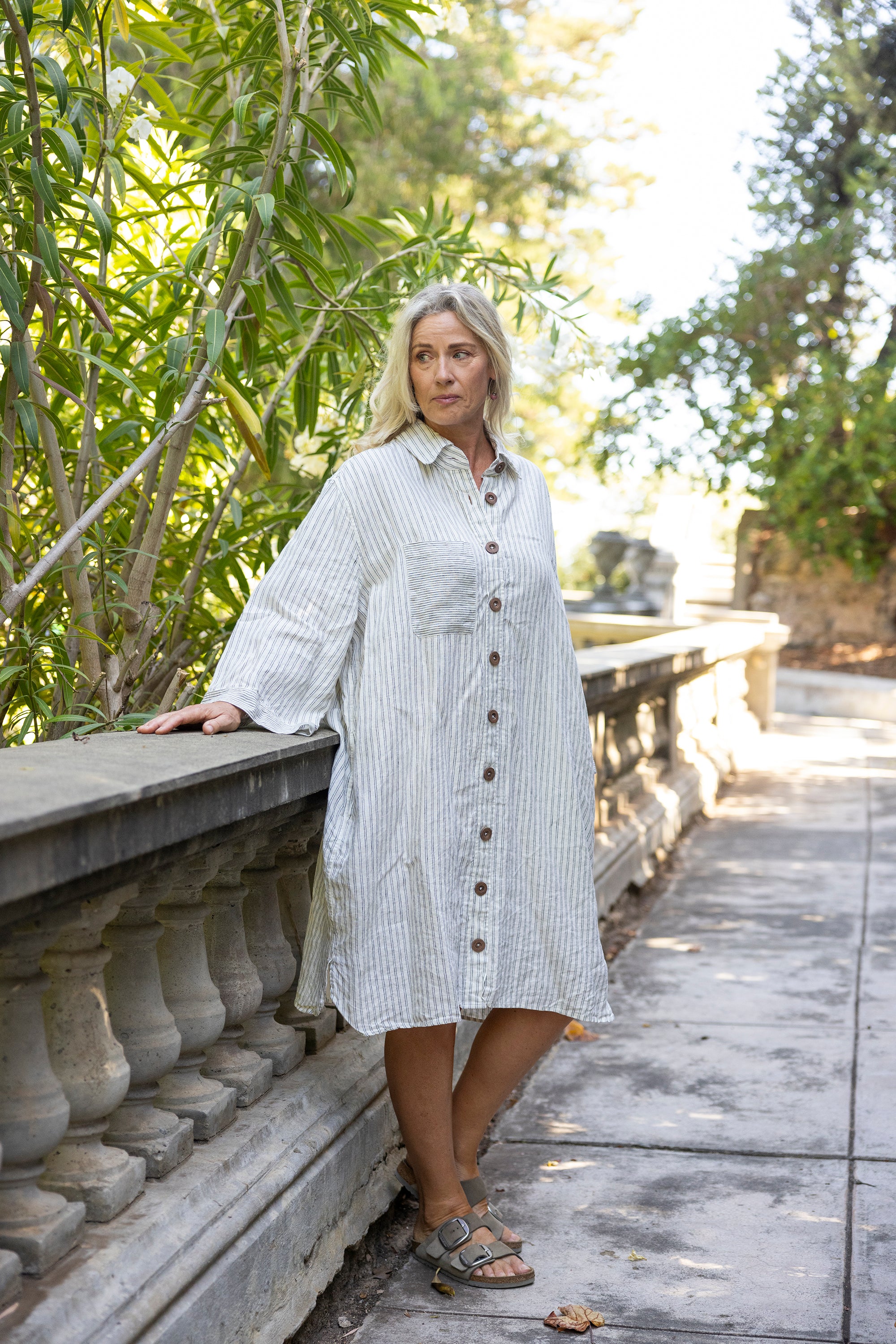 Woman in a white striped dress standing on a wooden path with greenery in the background