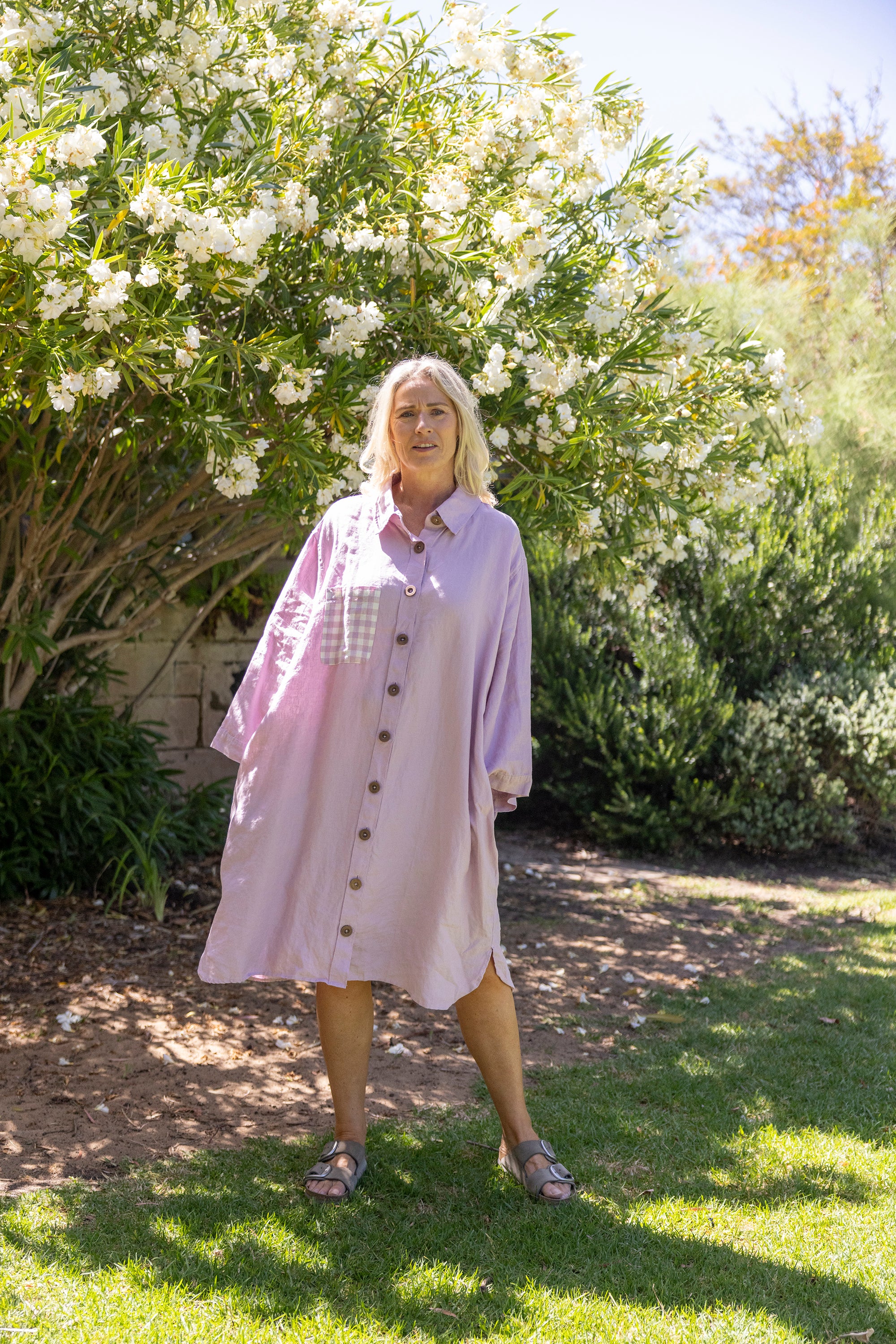 Woman in a light pink dress standing in a garden with white flowers and greenery.