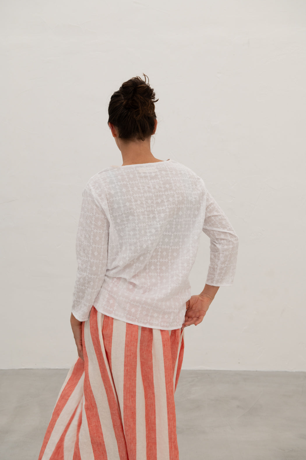 Woman wearing an embroidered white cotton boxy top with a relaxed fit and drop shoulders, from behind, paired with a red and white striped skirt