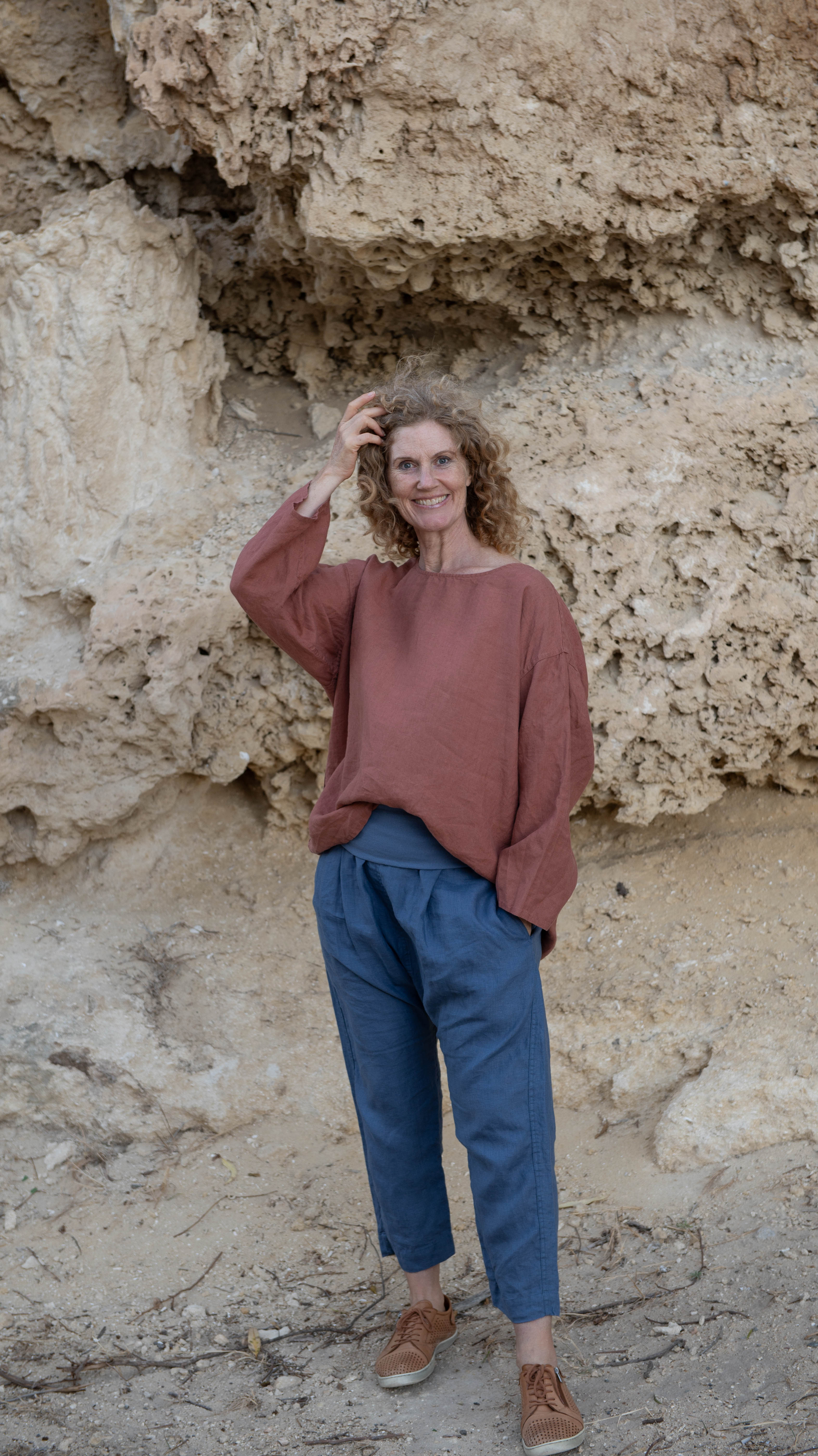 A woman standing outdoors wearing a relaxed fit, long-sleeved Boxy Top in a rust color, paired with dark pants.