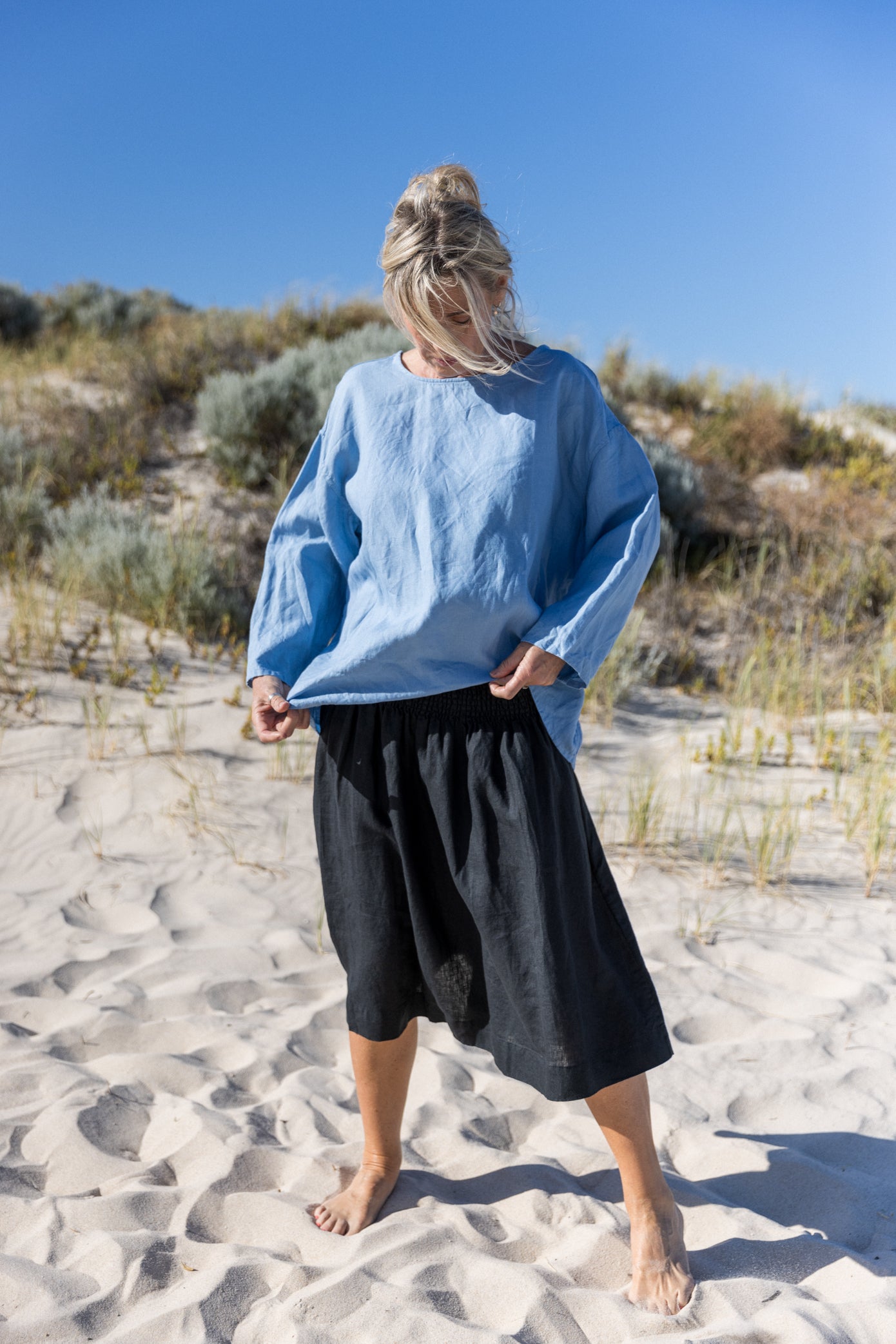 Woman standing outdoors on a beach wearing a relaxed-fit boxy top in a sky blue colour paired with a dark navy skirt