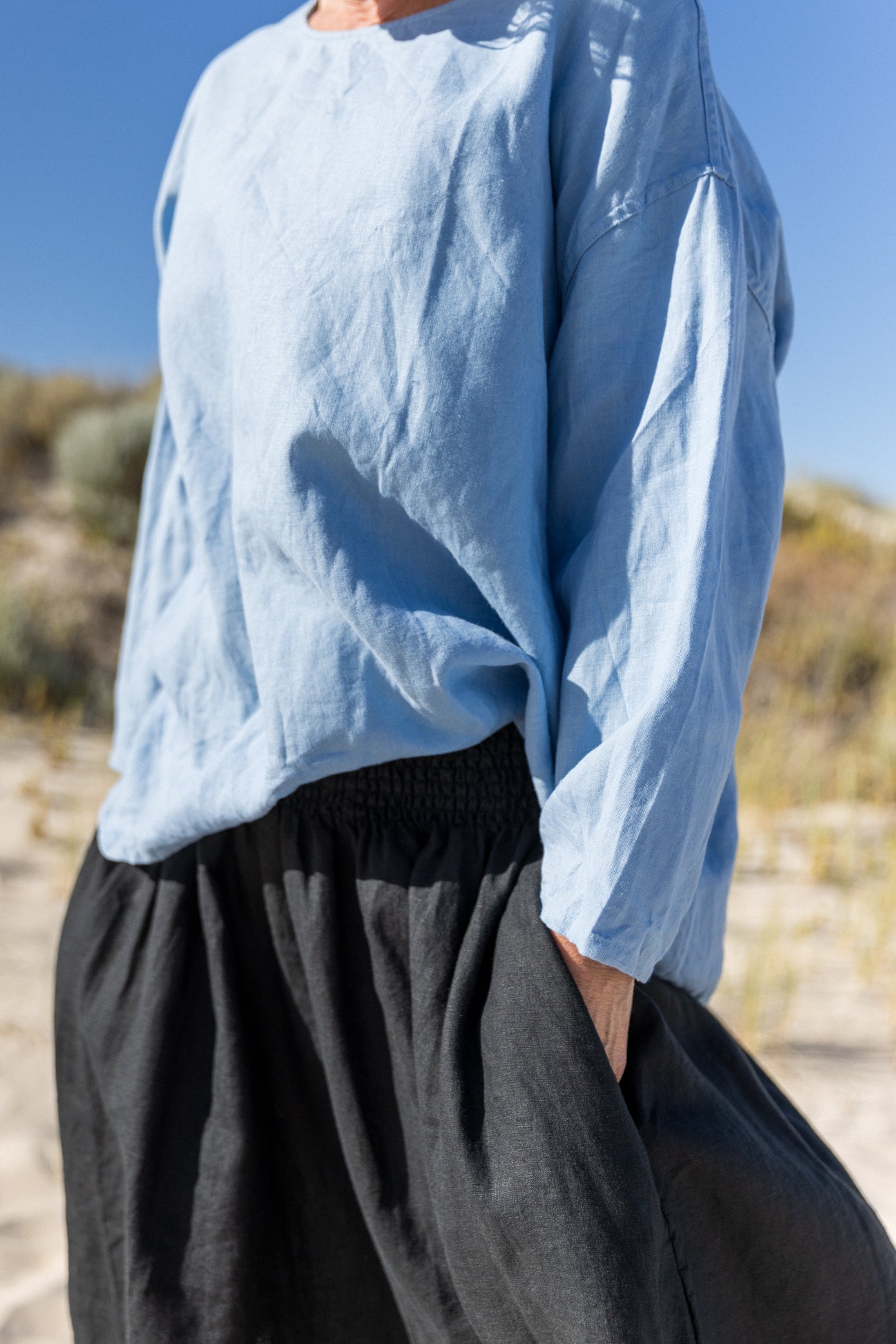 A woman standing outdoors wearing a relaxed fit, long-sleeved Boxy Top in a sky blue color, paired with dark blue skirt.