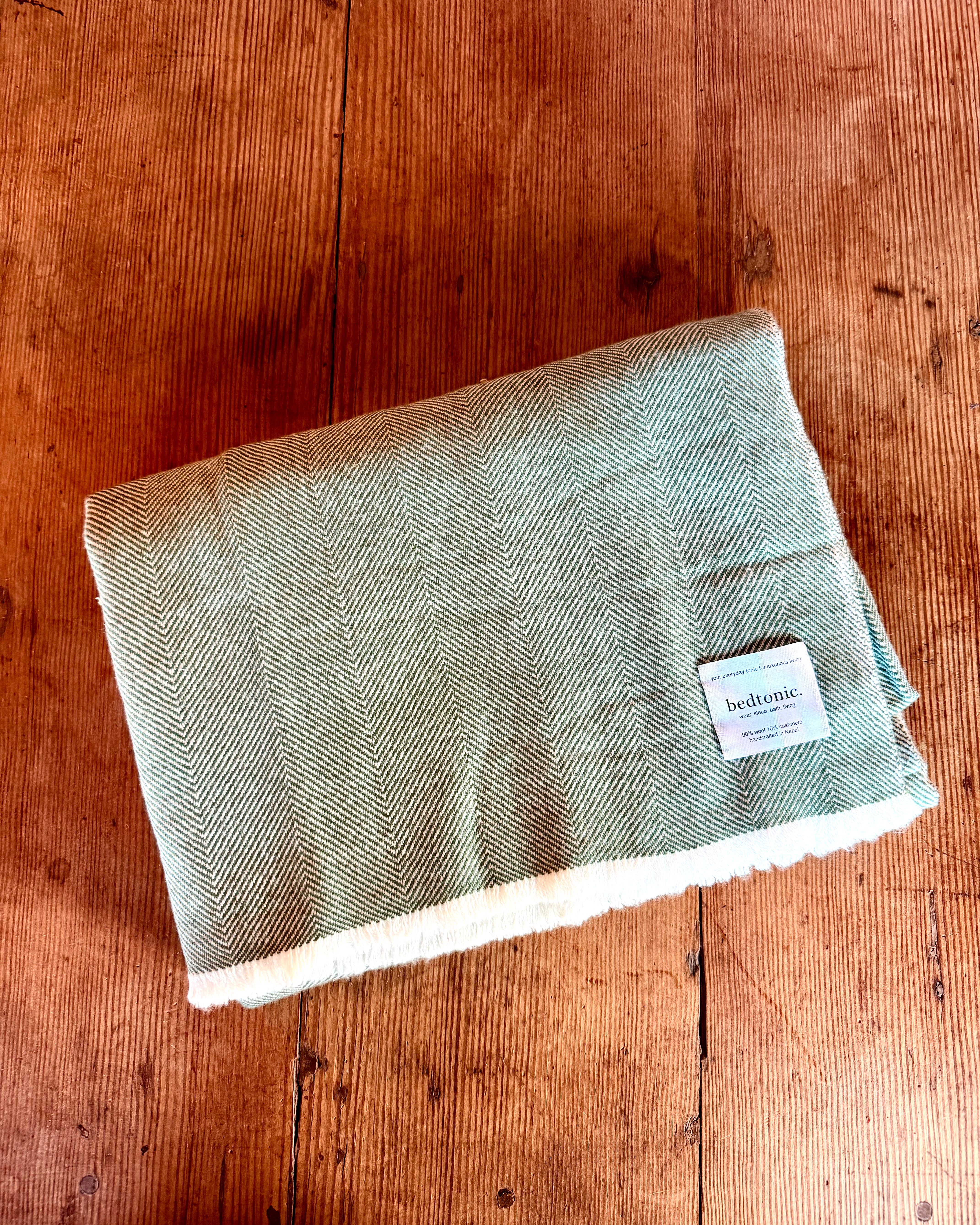 Moss green wool-cashmere throw blanket with chevron pattern and fringed edges, folded