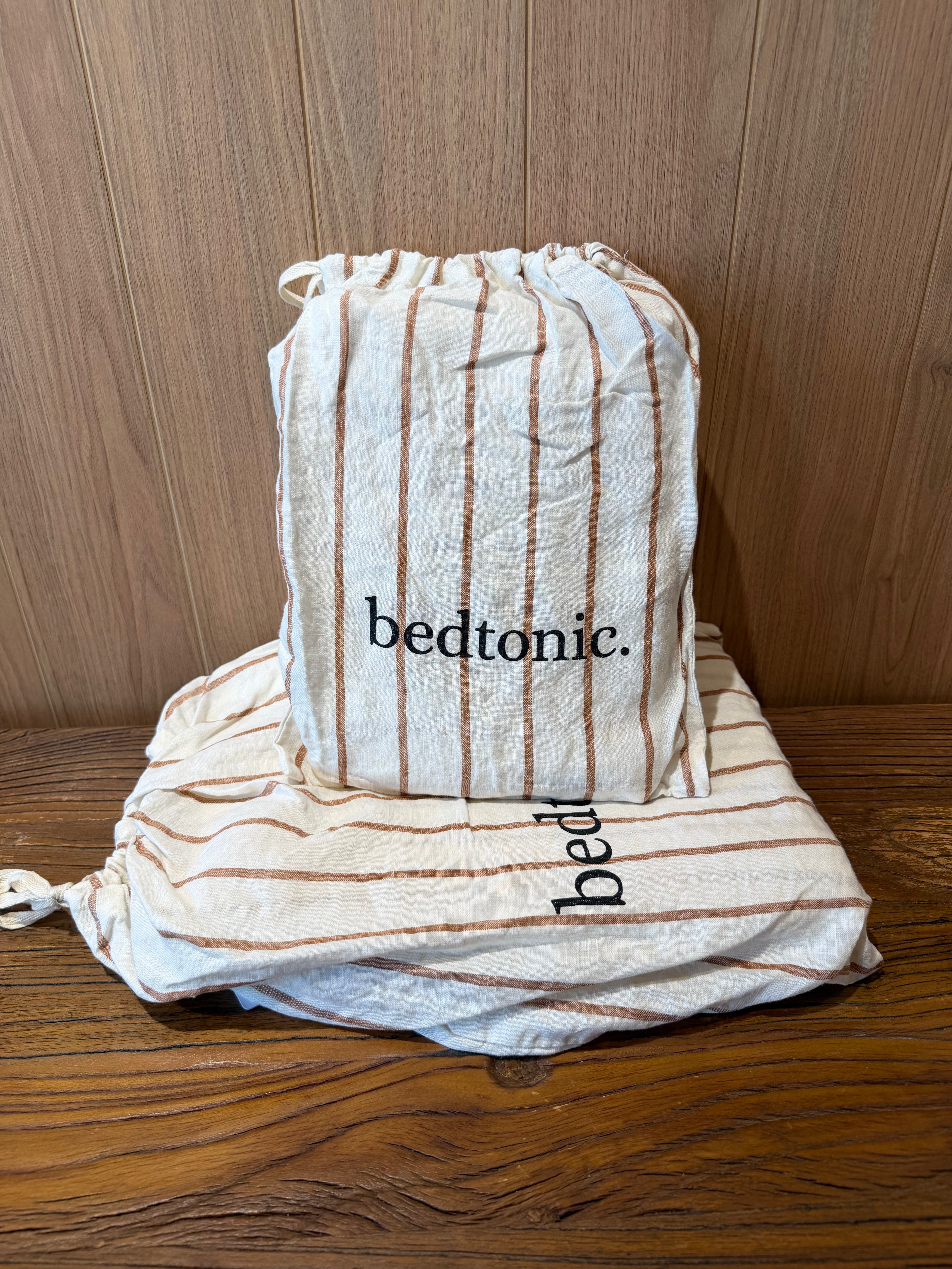 Linen flat sheet with ginger vertical stripes, folded with drawstring bag